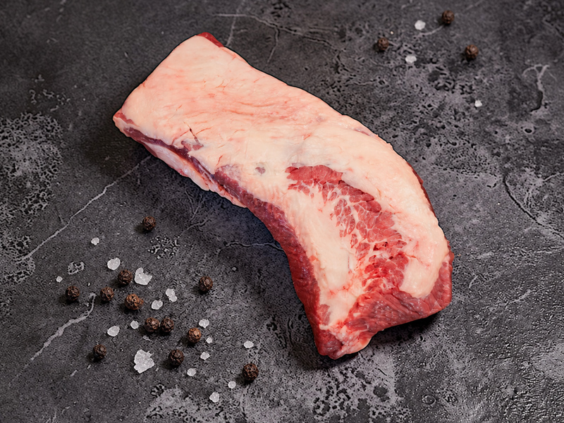 Rohes Black Angus Beef Brisket mit Fettabdeckung, grobem Salz und Pfefferkörnern auf dunkler Steinfläche
