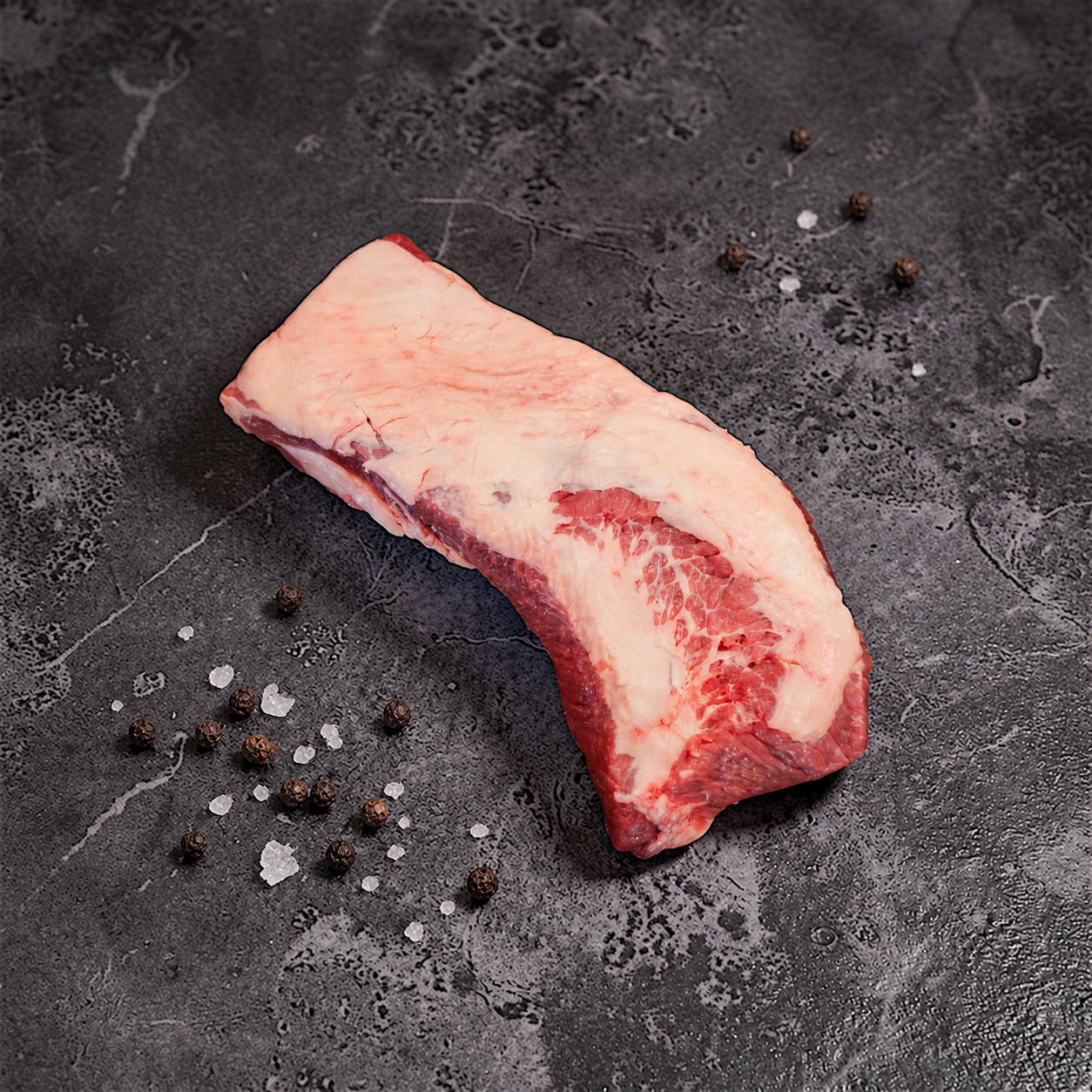 Rohes Black Angus Beef Brisket mit Fettabdeckung, grobem Salz und Pfefferkörnern auf dunkler Steinfläche